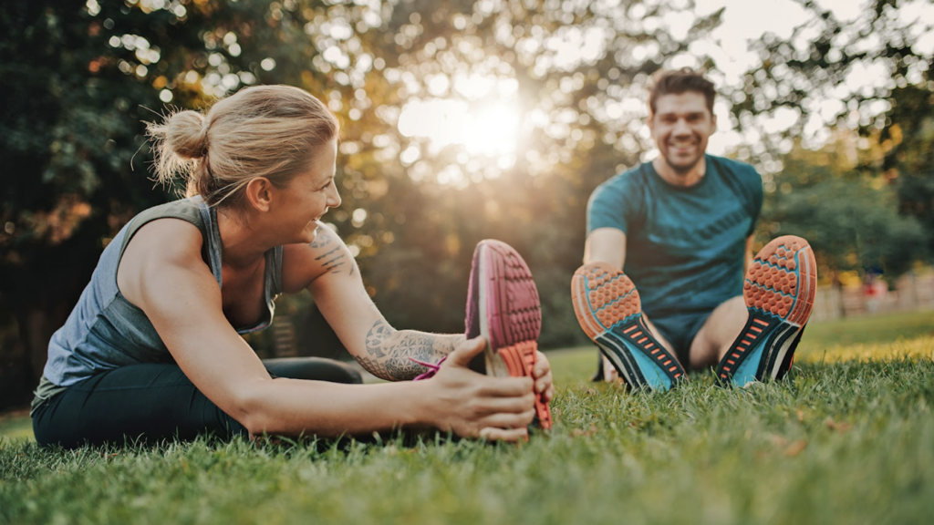 A man and a woman stretching in the grass, wearing workout clothing